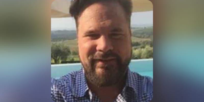 Chris in a blue check shirt by lakeside.